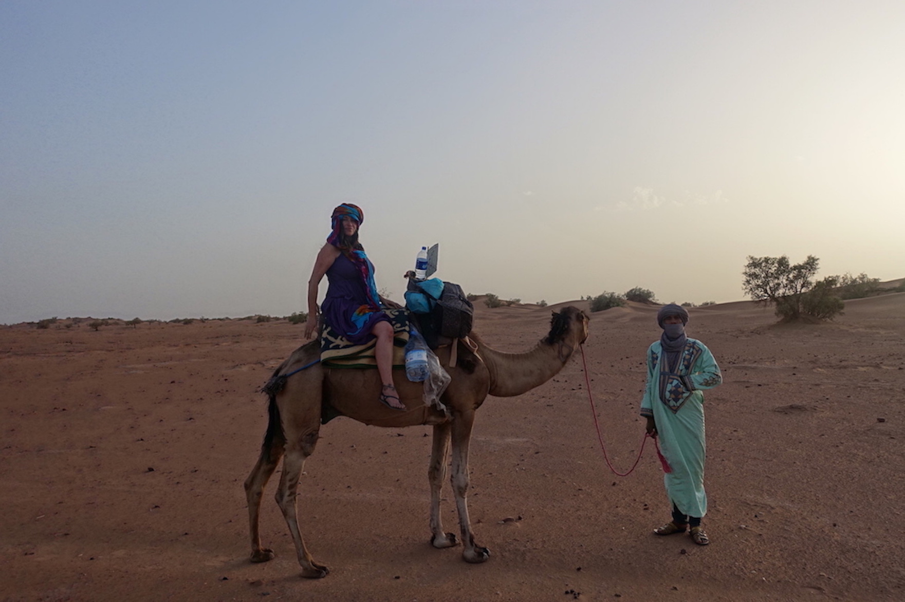 Pilar riding a camel and a guide on the front of the camel in the desert on the way to Erg Lihoudi