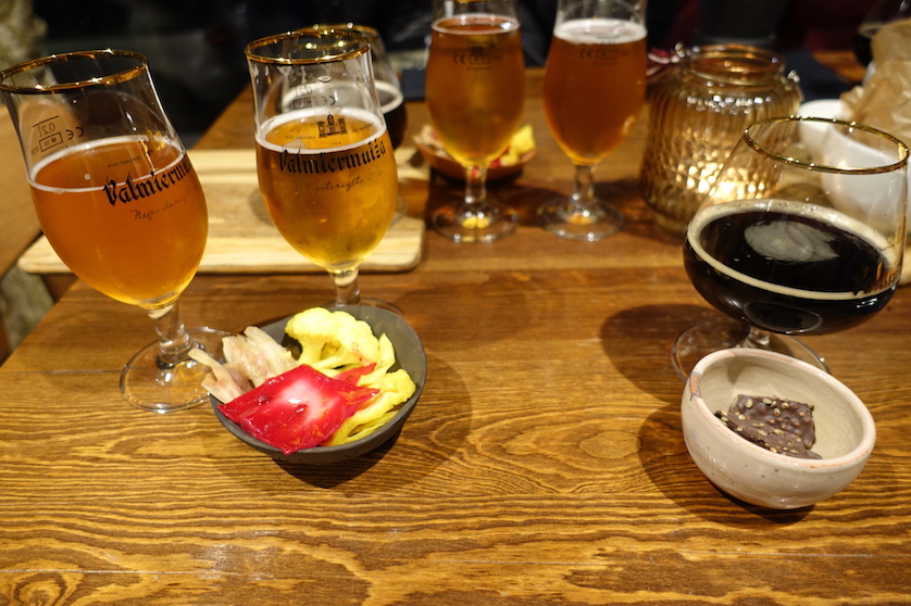 Different beers and snacks at a table. Four glasses of golden color beer and one glass of black beer.