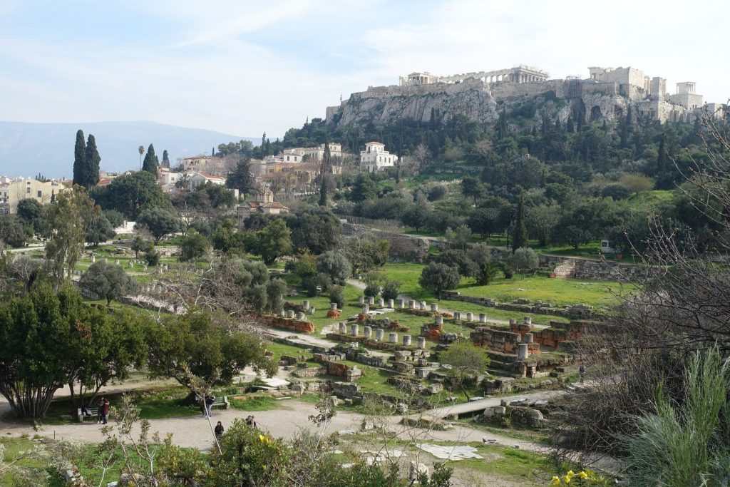 Kerameikos cemetery and acropolis hill. There are a lot of greenery and trees in between the ruins.