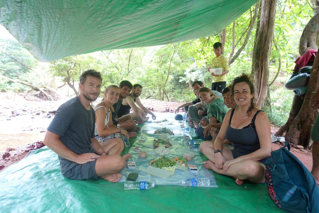 The whole tour group having lunch together. Sitting on the floor on a top of a green plastic carpet