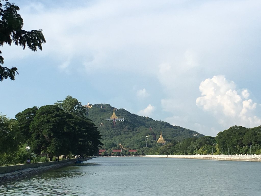 A view of the Mandalay hill and some Golden pagodas on the hill. You can see a body of water before the hill.