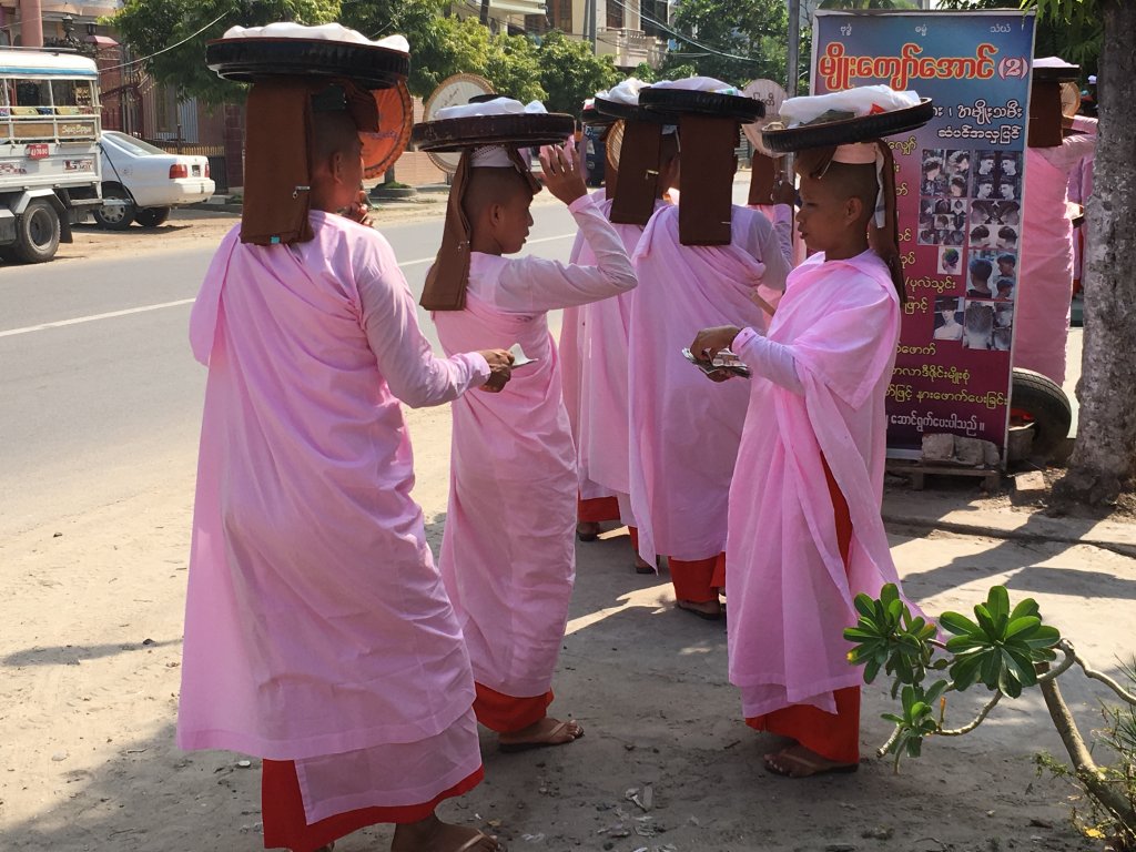 Buddhist Nuns receiving rice offerings. They are carrying the rice offerings on trays on their heads and wearing pink outfits.