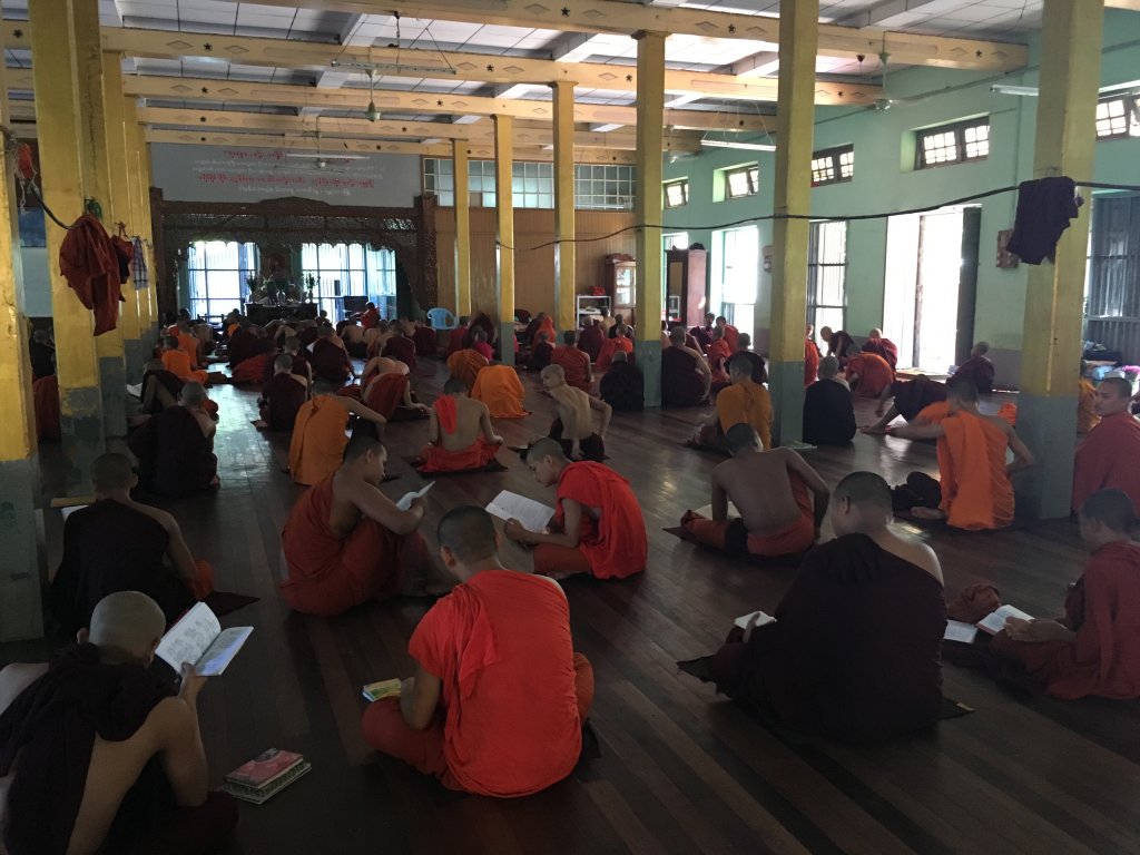 Many Buddhist monks taking a lesson on Buddhism. They are dressed in orange and some of them have taken off the top part of their dress