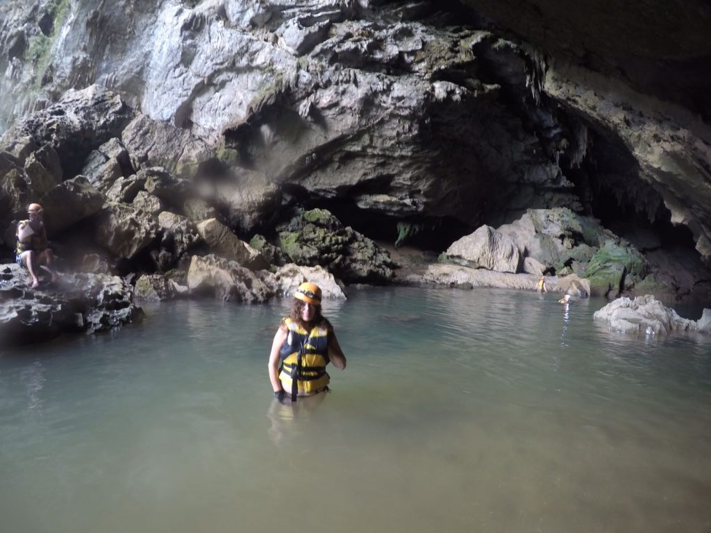 Pilar inside the water at the entrance of Tra Ang cave. She is wearing a yellow life jacket and a yellow helmet.