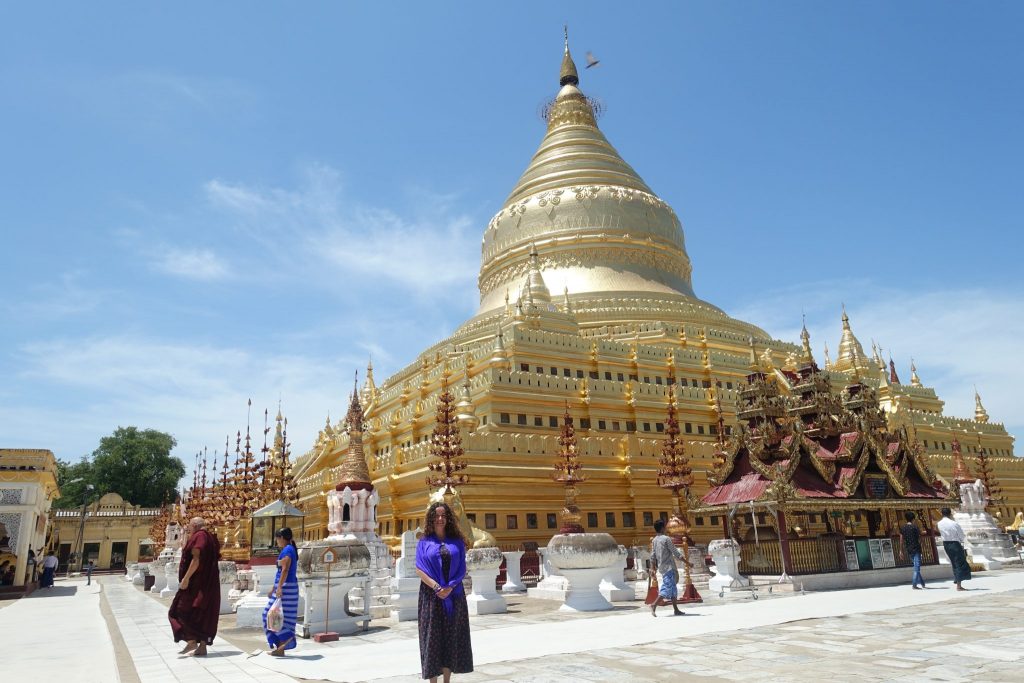 The golden Shewezigon pagoda and Pilar on the front of it. There are some people walking around the pagodas as well.