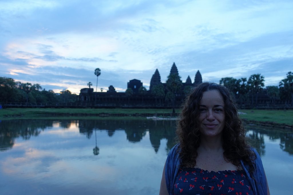 Pilar standing at the front of the Angkor Wat temple pond at sunrise.  You can see Angkor Wat temple complex at the back