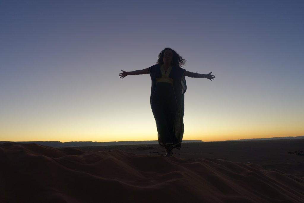 Pilar with open arms and the sunset light behind in the Tinfou dunes