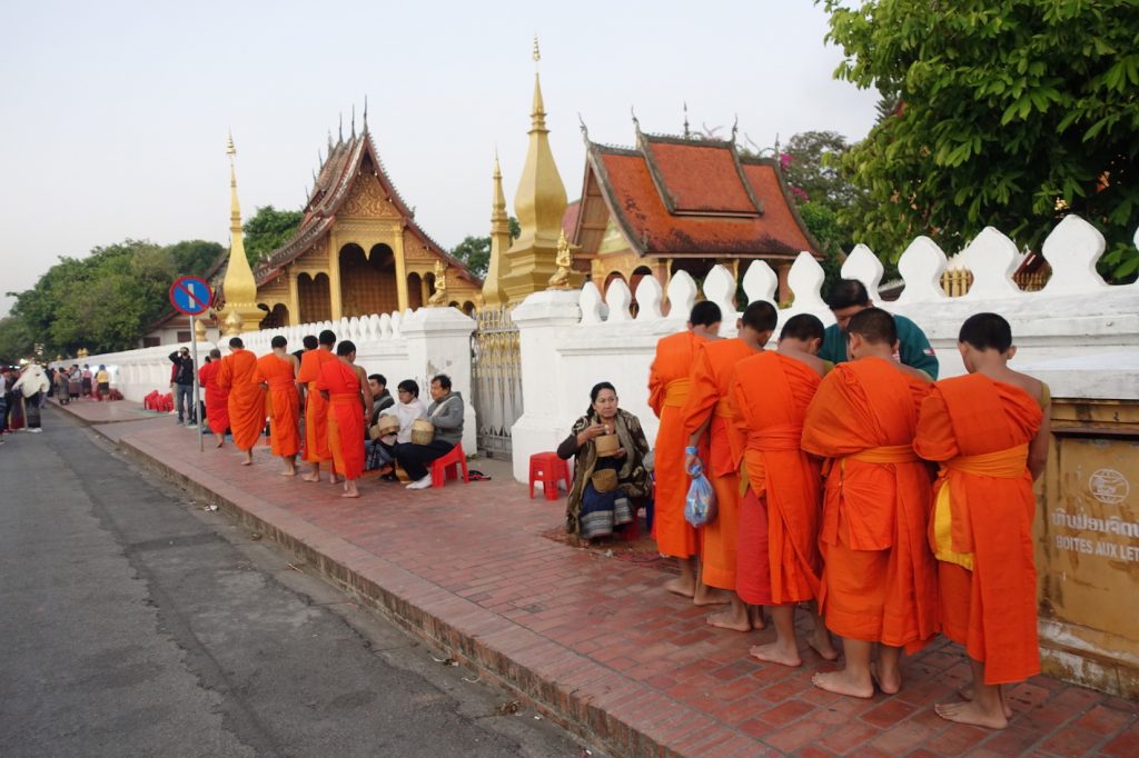 Arow of Buddhist monks in front of a temple during the alms giving ceremony. They are receiving rice from the people
