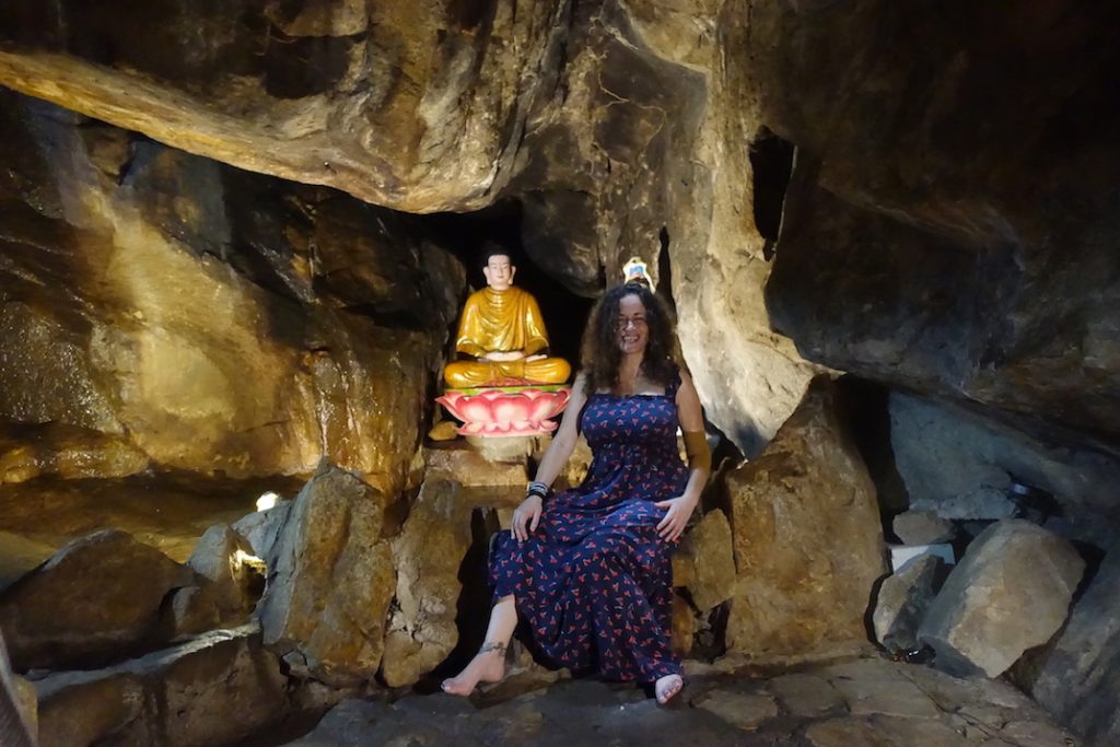 Pilar sitting close to a Buddha image inside the cave Pagoda in Chau Doc