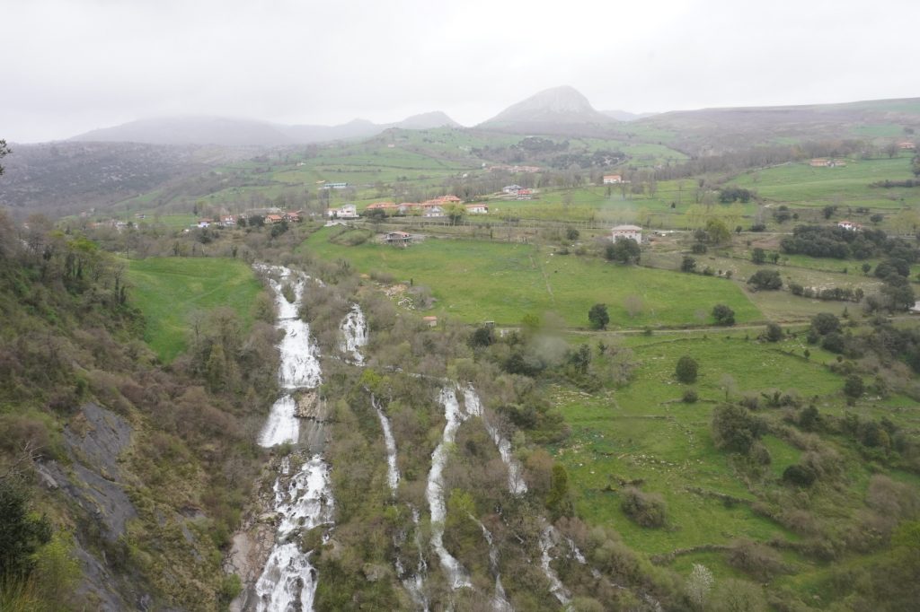 La Gandara waterfall. A view of the village of La Gandara, the mountains on the back and a lot of green fields and the waterfall