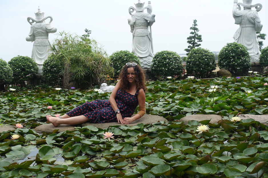 Pilar sitting on a rock in the middle of many floating Lotus flowers.  There are some white status on the back.