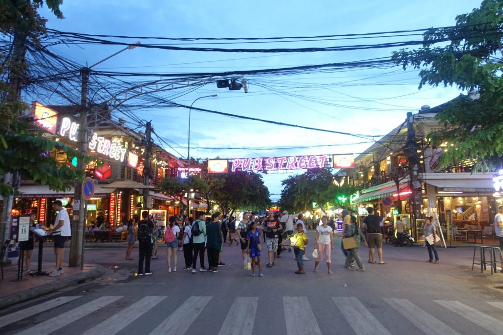 A photo at dawn of Pub Street with a lot of colorful lights and pubs on both sides and people walking on the streets