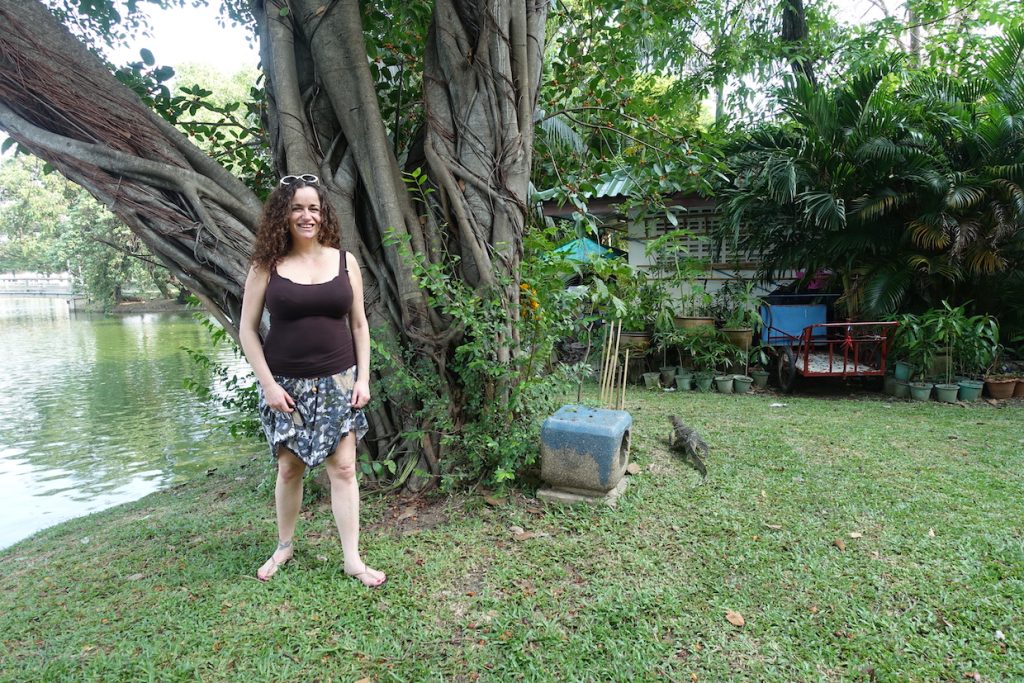 Pilar standing in front of a tree and a monitor lizar on the back of the tree in the Lumpini park in Bangkok
