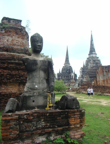 A Buddha statue with only one arm and two towers on the background. This is located in Ayutthaya, the former capital of Thailand