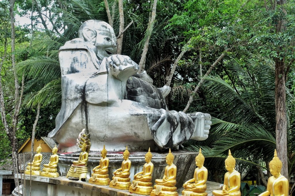 A big laughing Buddha image in grey color and a line of golden Buddhas on the egde where the big Buddha is located
