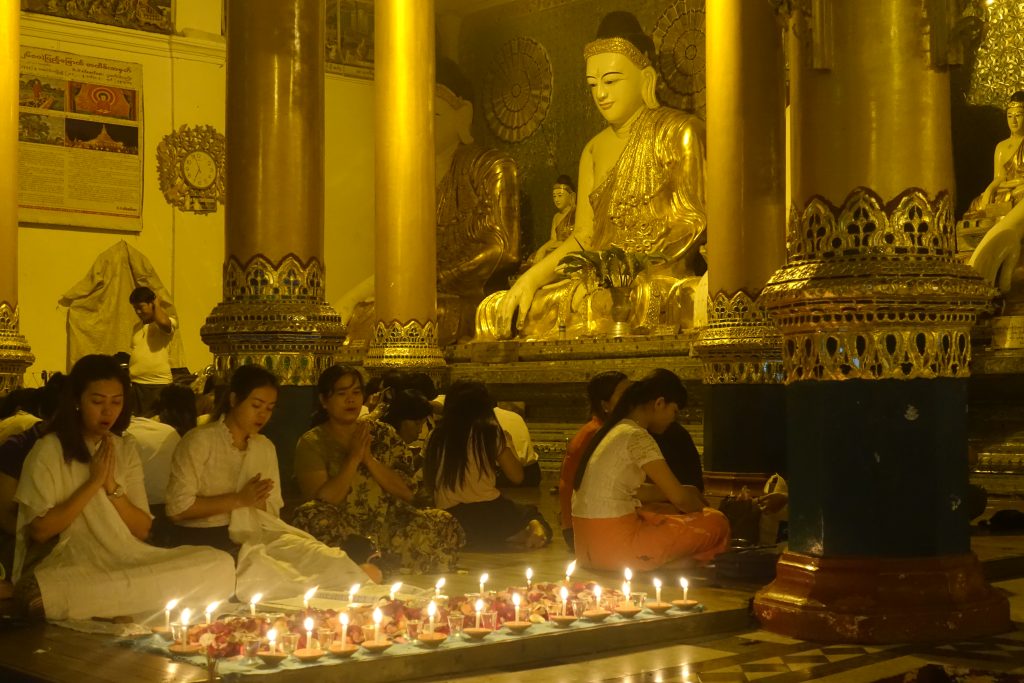 Some woman in prayer with many candles and a Buddha statue in the Shwedagon pagoda. in Myanmar