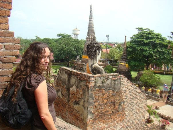Pilar looking side ways on top of one of the temples in Ayutthaya. You can see a tower and the head of a Buddha on the background of the picture.