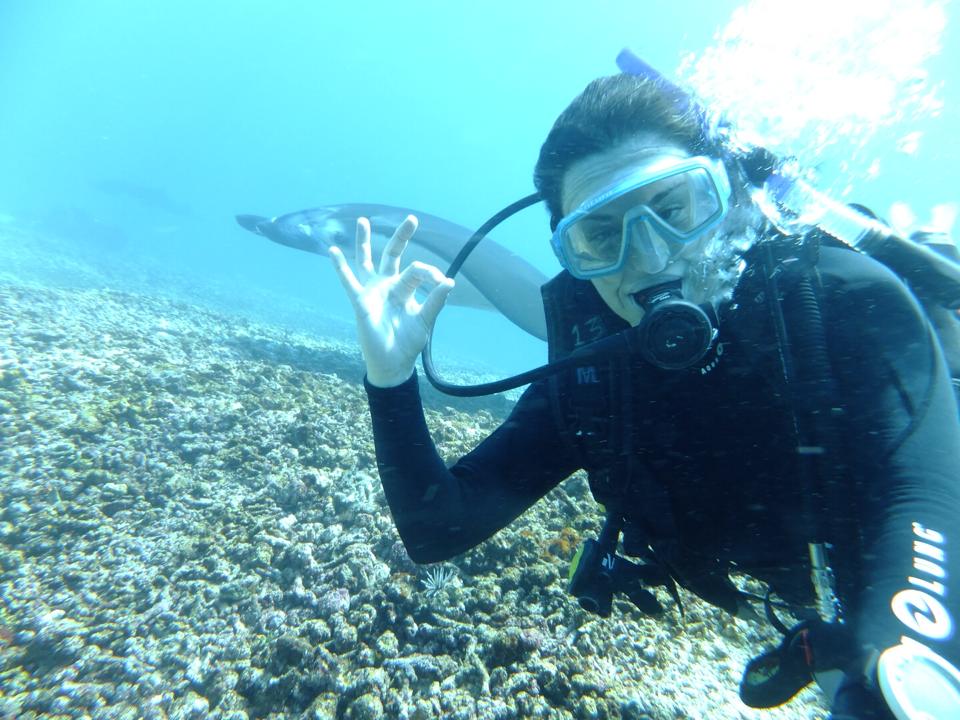 Pilar scuba diving with a manta Ray on the back making the OK sign with her hand