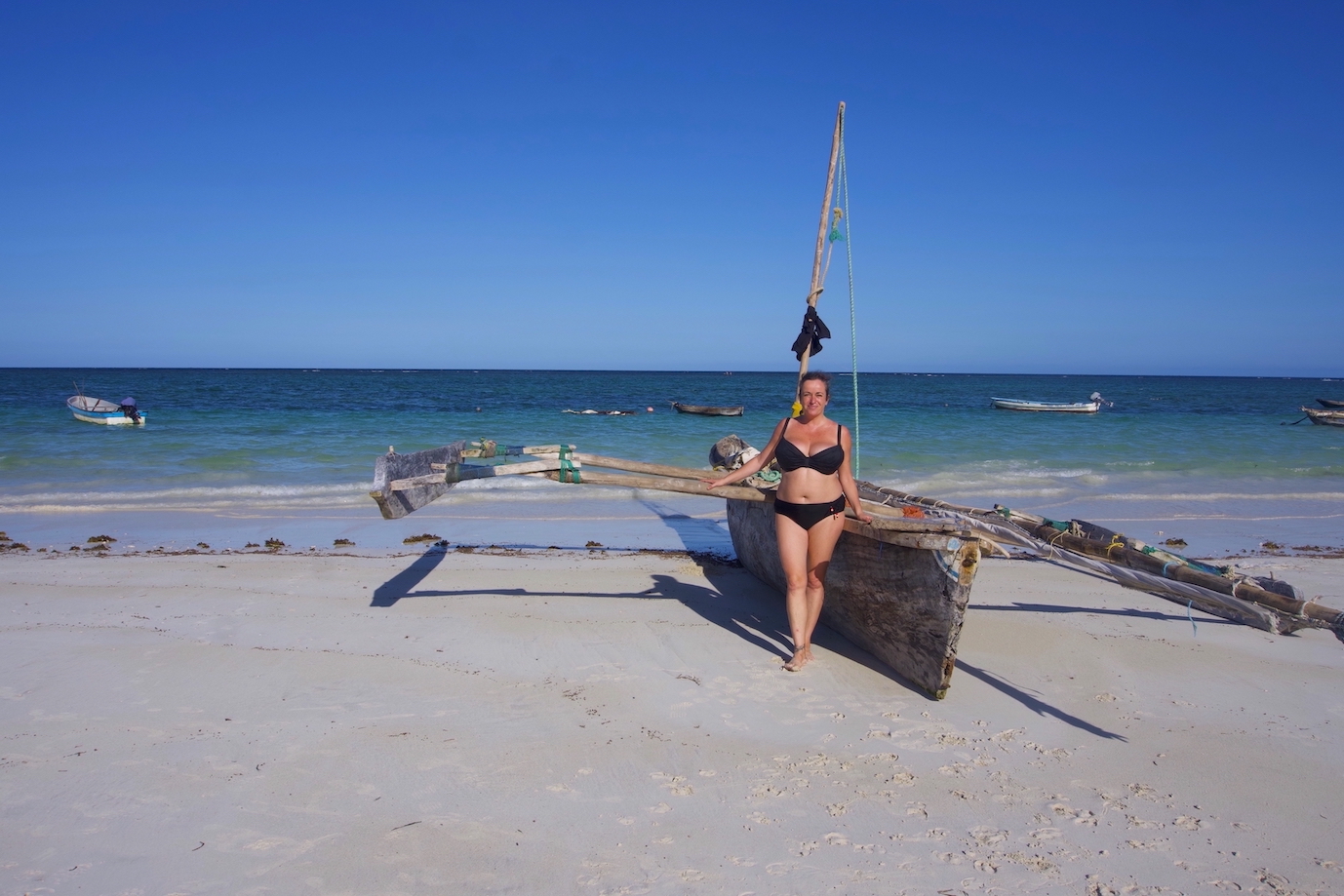 Pilar leaning on a two winged boat in Diani beach with sea and some other boats on the background