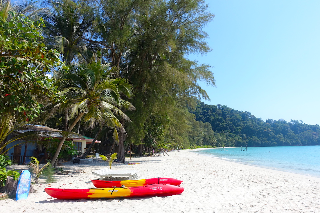 Neverland beach, Koh Kood. A view of the palm trees, two red and yellow boats and the crystaline emerald water.