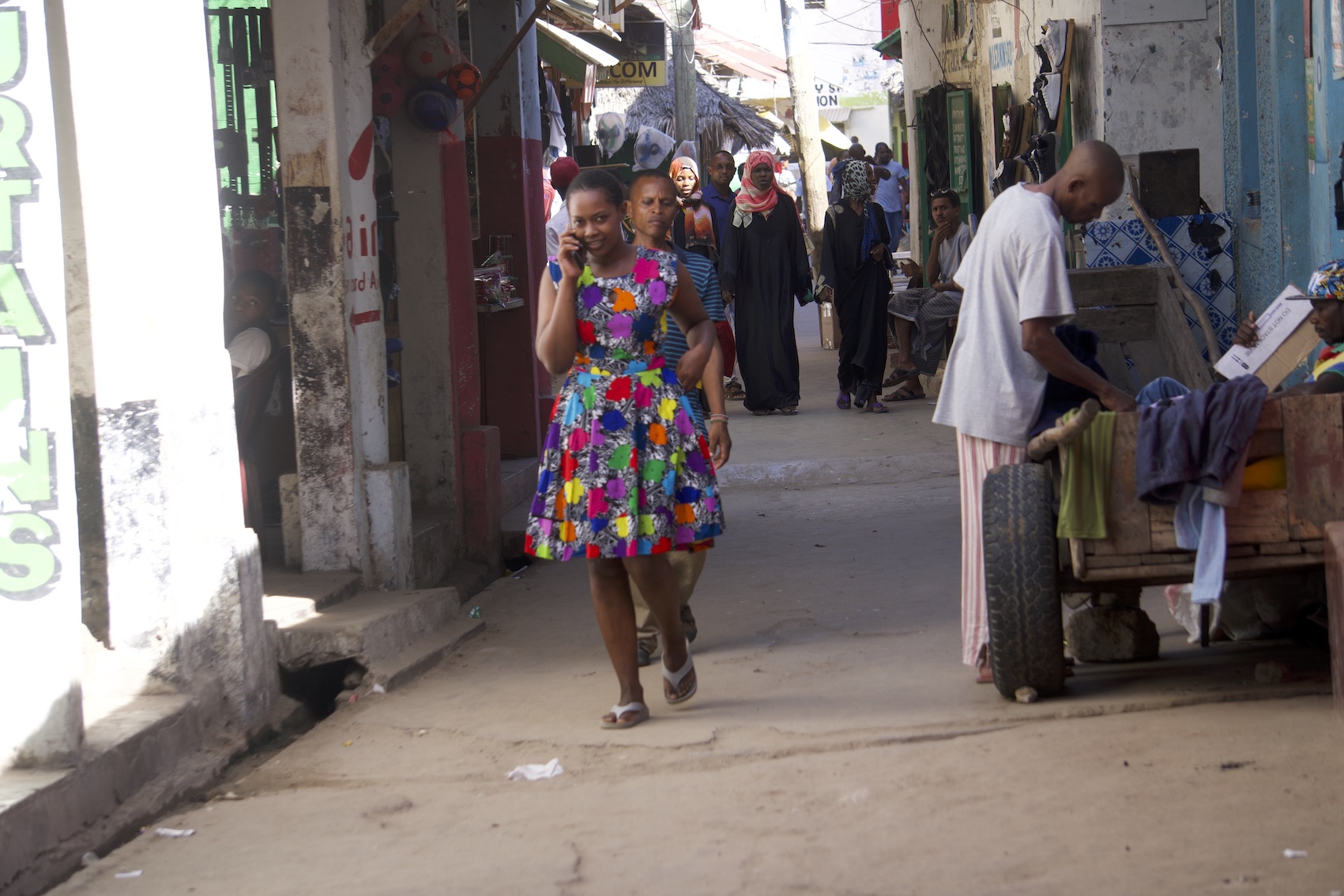 People walking on Lamu Old Town, lady in colorful dress with a phone