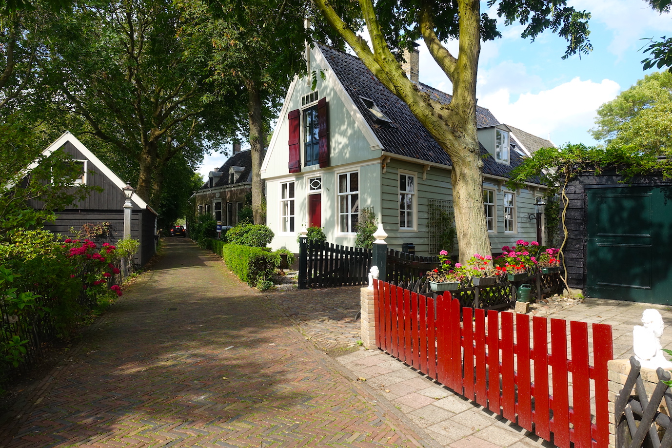 A street with wooden houses a red fence and some colorful flowers gardens in Broek in Waterland