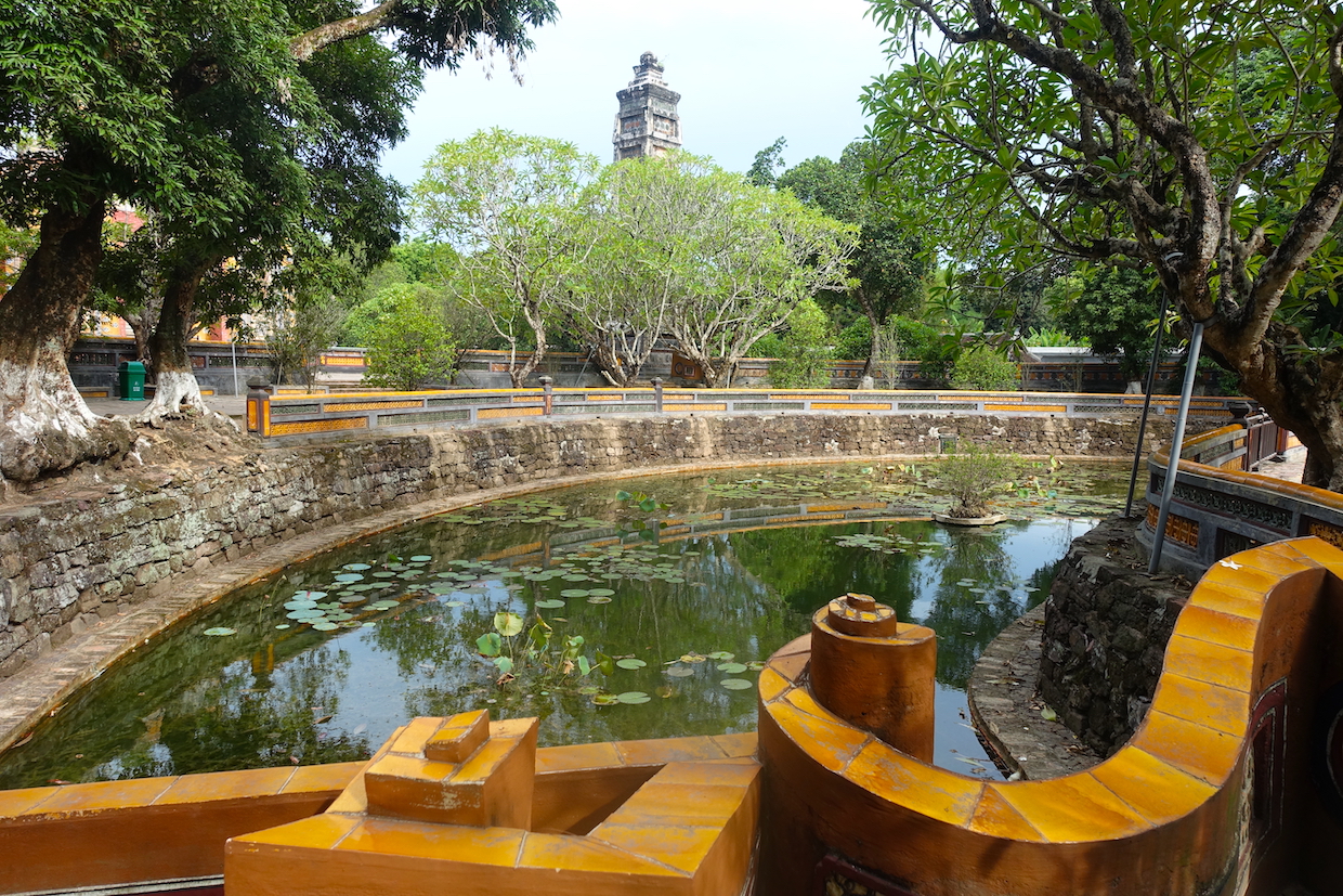 A view of a brown bridge and a pond with lotus flowers at the Tu Duc tomb in Hue