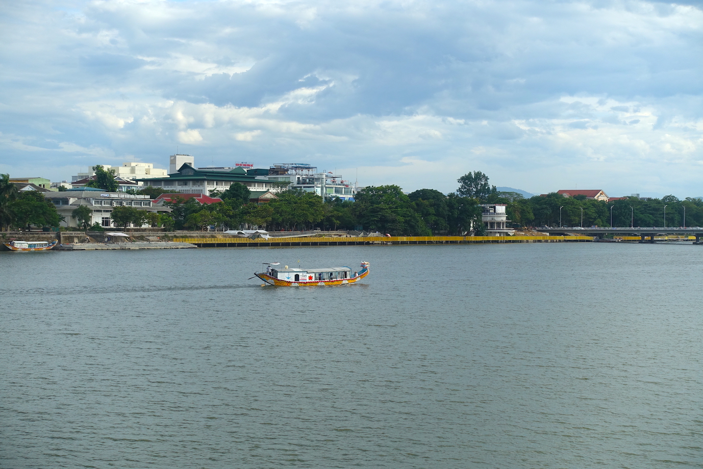 A view of the perfume river, some buildings and a boat crossing the river