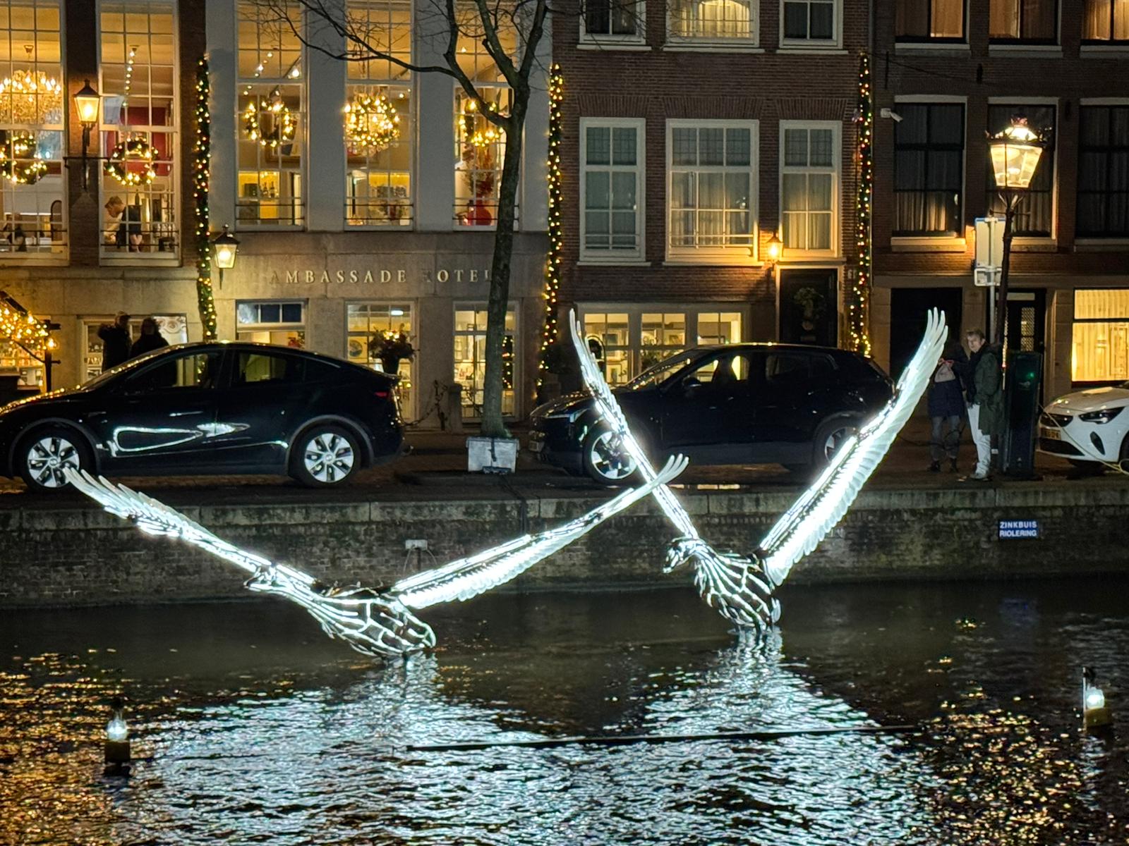 Illuminated swan light sculptures floating on an Amsterdam canal during the Amsterdam Light Festival in December.