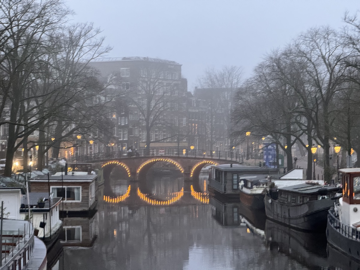 Foggy Amsterdam canal with glowing bridge lights creating a mysterious scene often featured in haunted city legends.