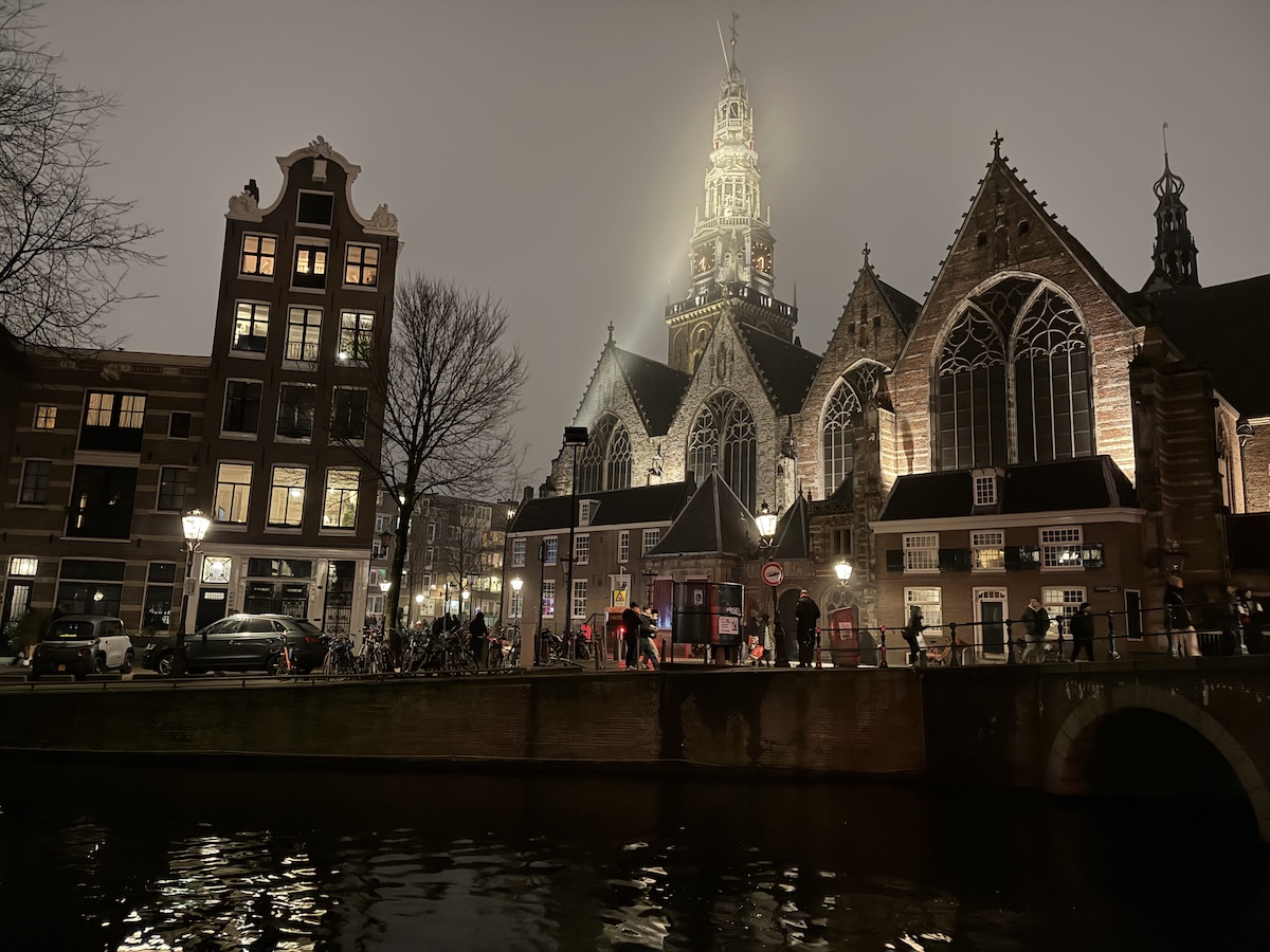 Oude Kerk church tower rising into the mist at night in Amsterdam’s Red Light District during a ghost walk.