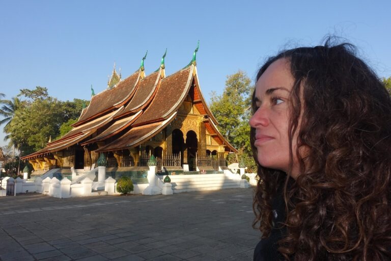 Wat Xieng Thong temple in Luang Prabang, Laos, with traditional Lao architecture and a visitor in the foreground.