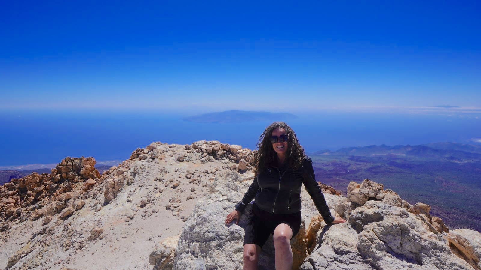 Traveler enjoying panoramic mountain and ocean views from a rocky summit